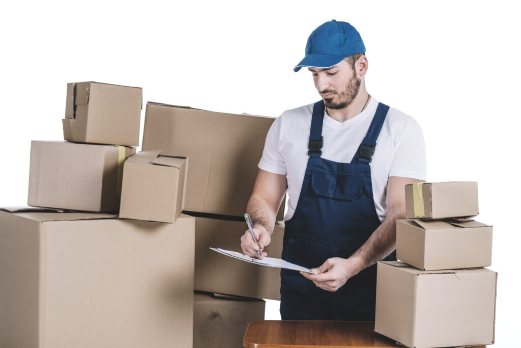 A logistics worker in a blue cap and overalls inspecting and organizing stacked cardboard boxes while holding a clipboard. The image represents efficient import/export management and supply chain solutions provided by Importivity.