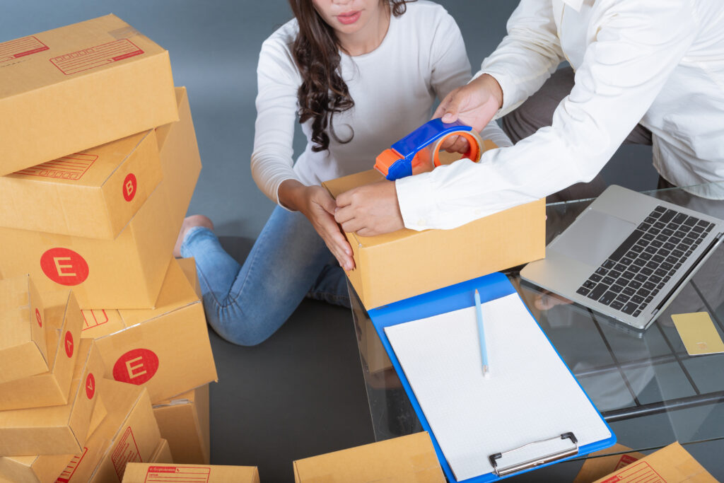 Two workers sealing and organizing shipping boxes with a clipboard nearby, representing streamlined supply chain management, packaging efficiency, and global logistics solutions.