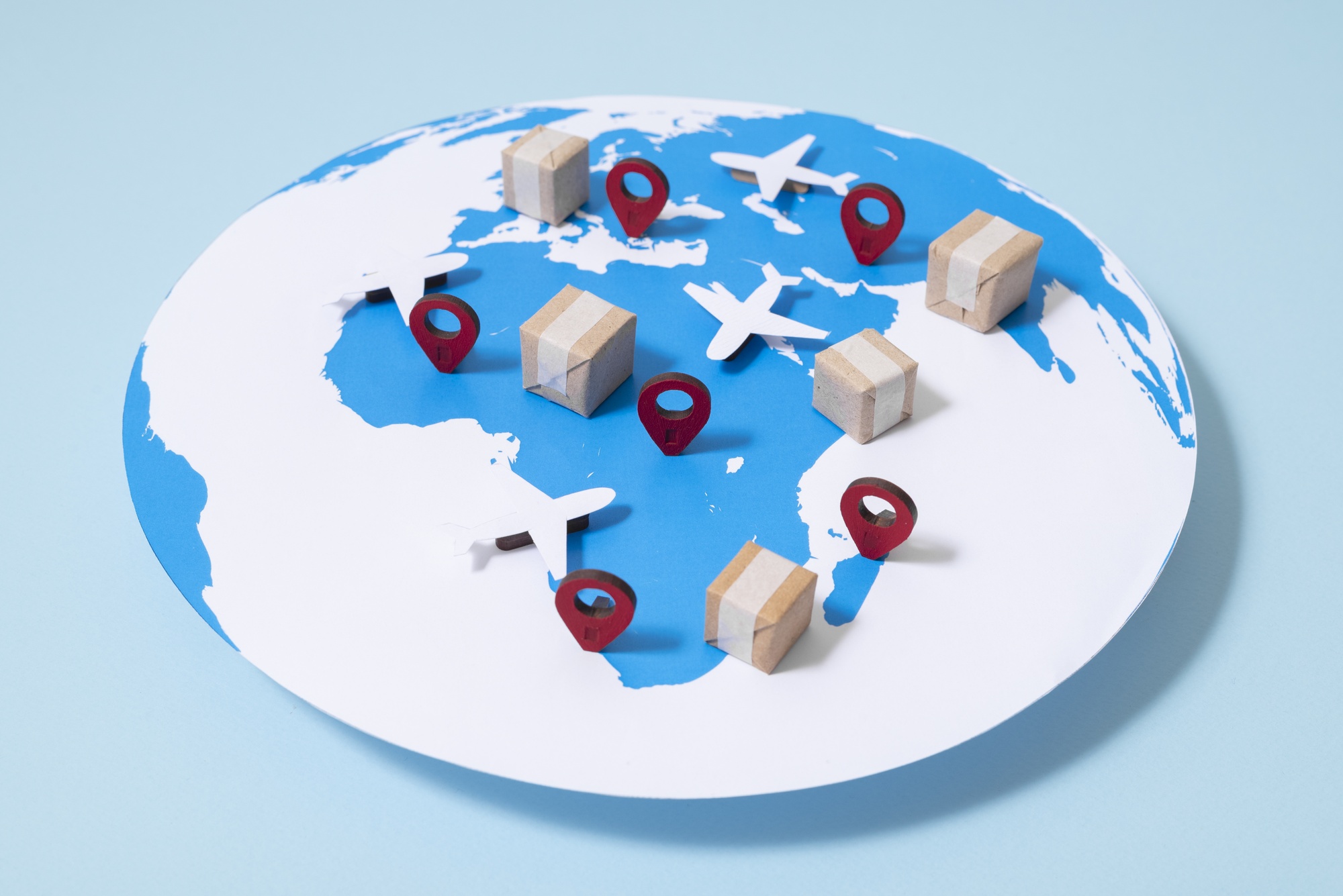A stylized world map featuring miniature airplanes, cardboard boxes, and red location pins, symbolizing international trade, global logistics, and seamless bulk purchasing solutions.