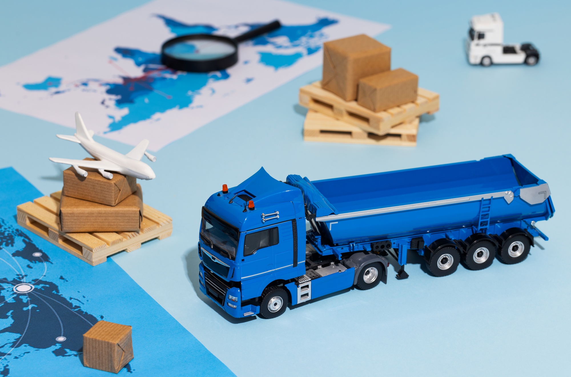 A miniature blue truck with stacked cardboard boxes on a stylized world map, symbolizing domestic supply chain efficiency, faster delivery, and premium goods sourcing within the United States.