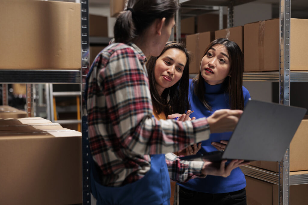 A group of warehouse workers engaged in a discussion surrounded by shelves stocked with boxes. The image represents teamwork, supply chain management, and bulk sourcing solutions from Mexico.