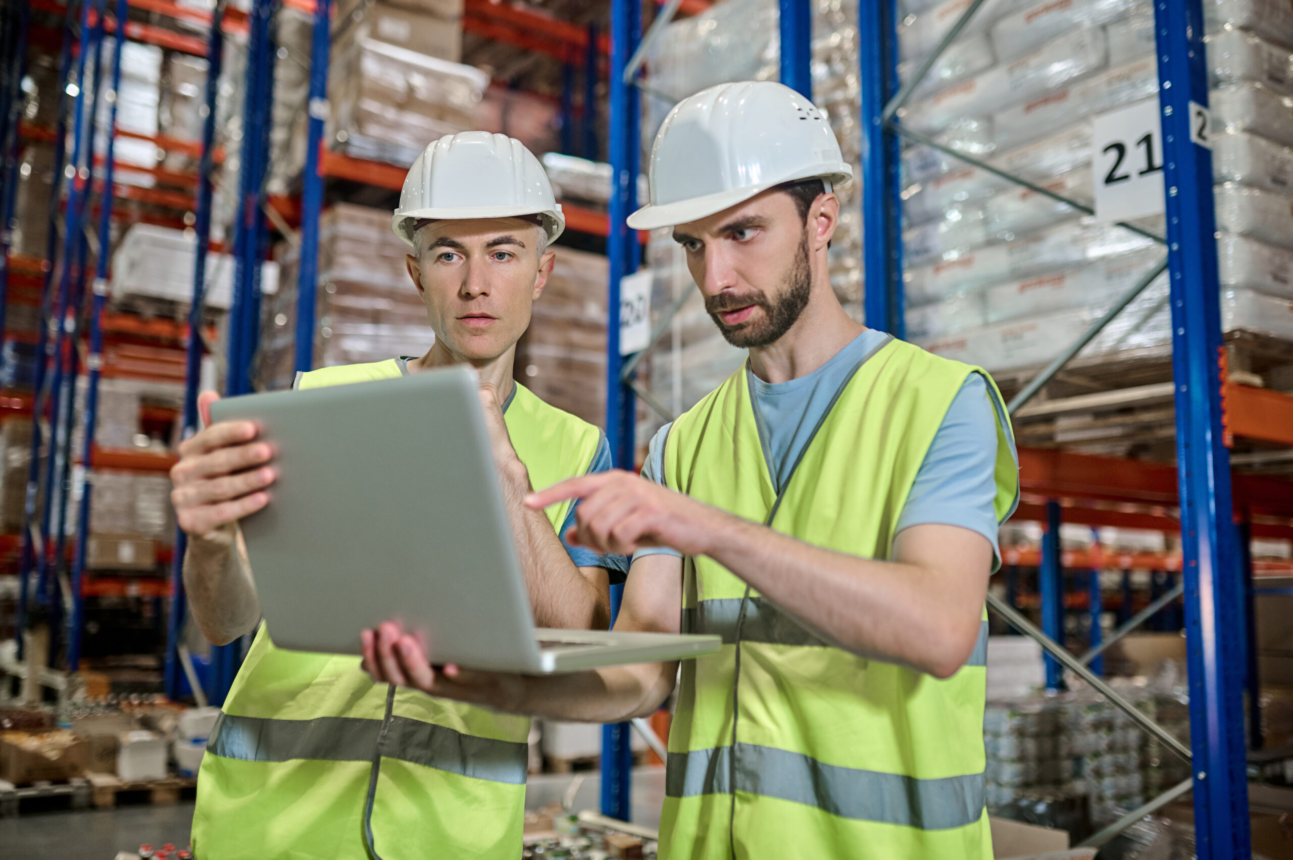 Two men looking at a laptop while deciding work tasks inside a warehouse.